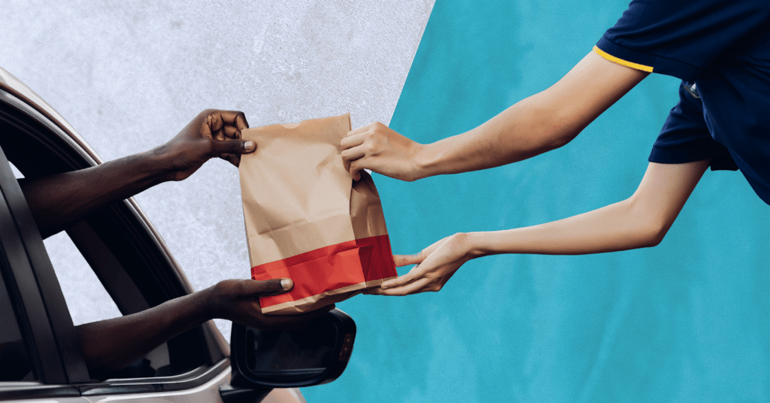 A worker handing a paper bag to a customer in a car.