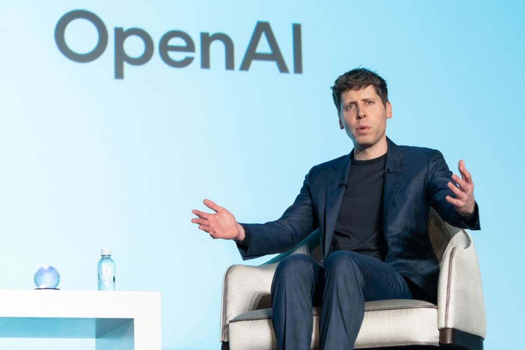 Sam Altman sitting in front of an OpenAI projection.