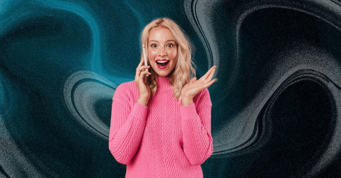 A woman in a pink sweater smiles as she talks on the phone.