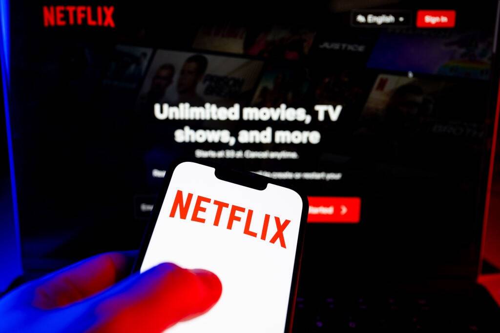 A Netflix logo on a smartphone in front of a TV.