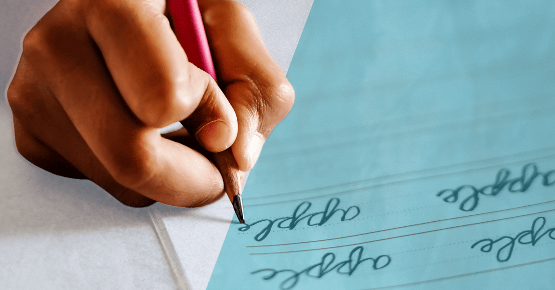 A hand holding a red pencil and writing in cursive.