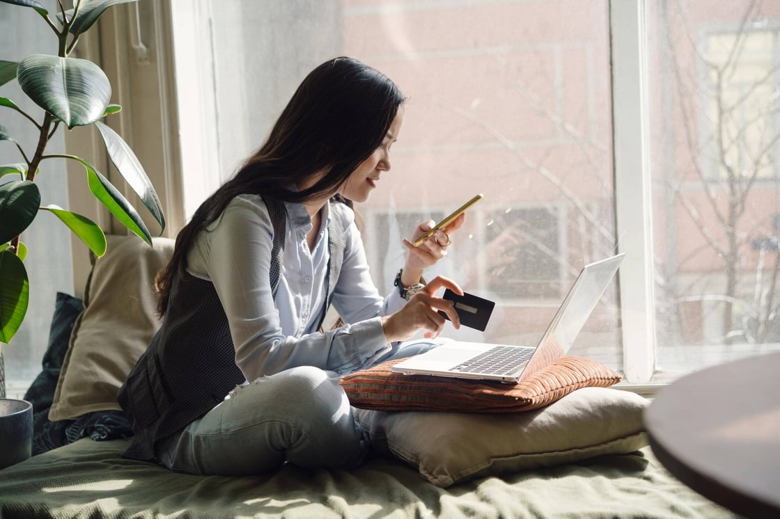 A woman holding a credit card and speaking on the phone in front of a laptop.