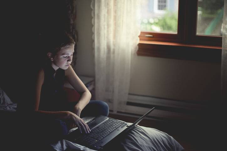 A teenage girl on her laptop in bed.