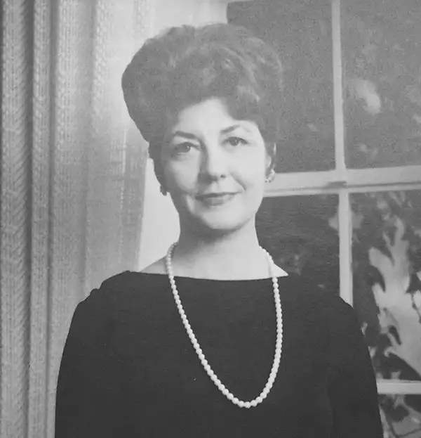 Black-and-white photo of Bette Nesmith Graham in a dark dress and pearl necklace, indoors with a window backdrop.