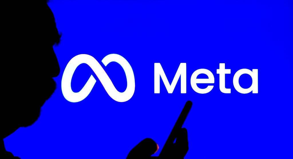 A man’s silhouette holding a phone against the Meta logo.