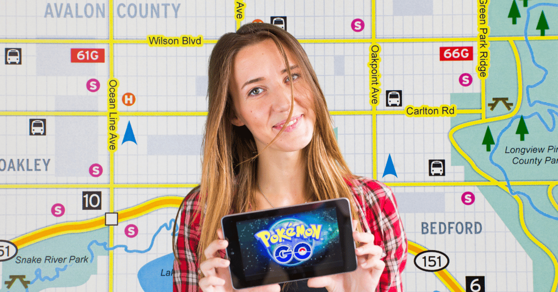 A woman holding a phone open to the Pokemon Go screen stands in front of a map.