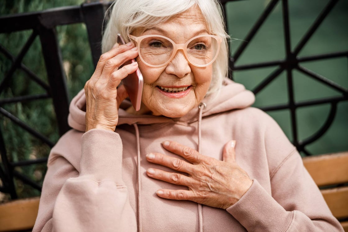 A woman with white hair talking on the phone and smiling.