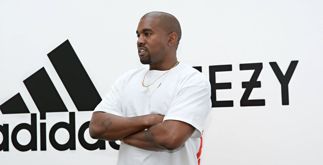 Ye stands in front of a white background with the Adidas and Yeezy logos.