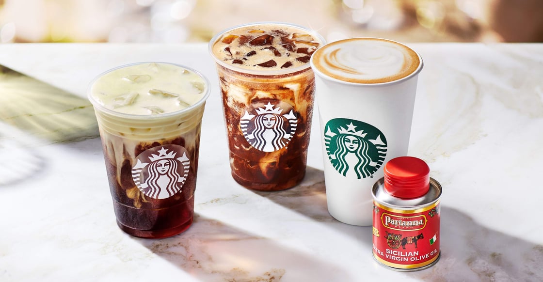 Three drinks from the Starbucks Oleato beverage line sit on a counter alongside a small can of Partanna extra virgin olive oil.