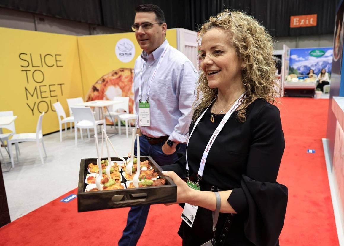 woman holding food samples on a serving tray in a convention-style environment