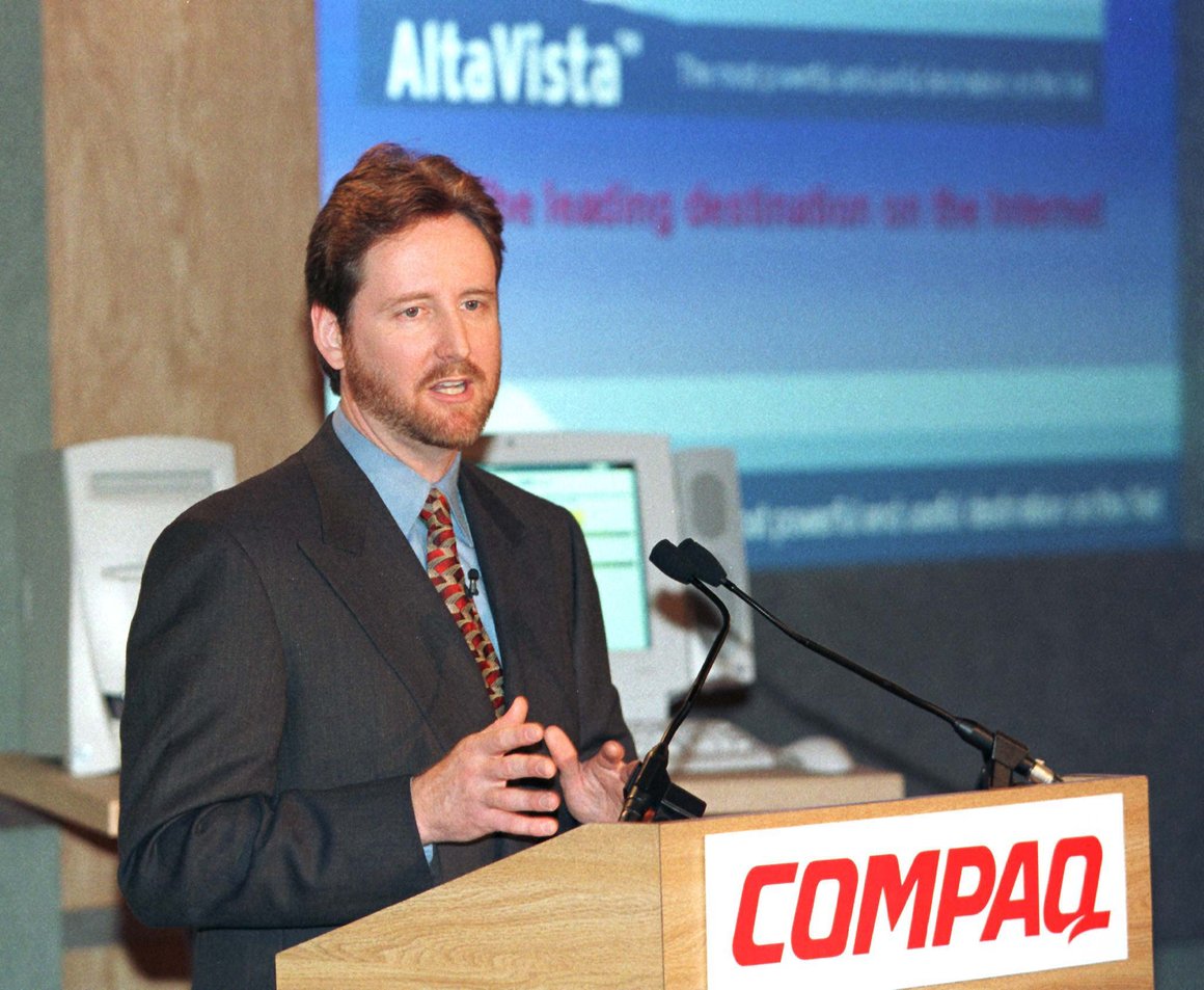 Man in suit standing at lectern displaying Compaq logo