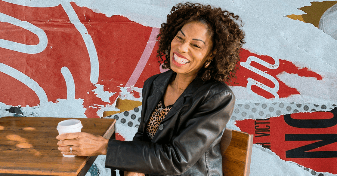 A smiling woman sits at a desk with a cup of coffee. 