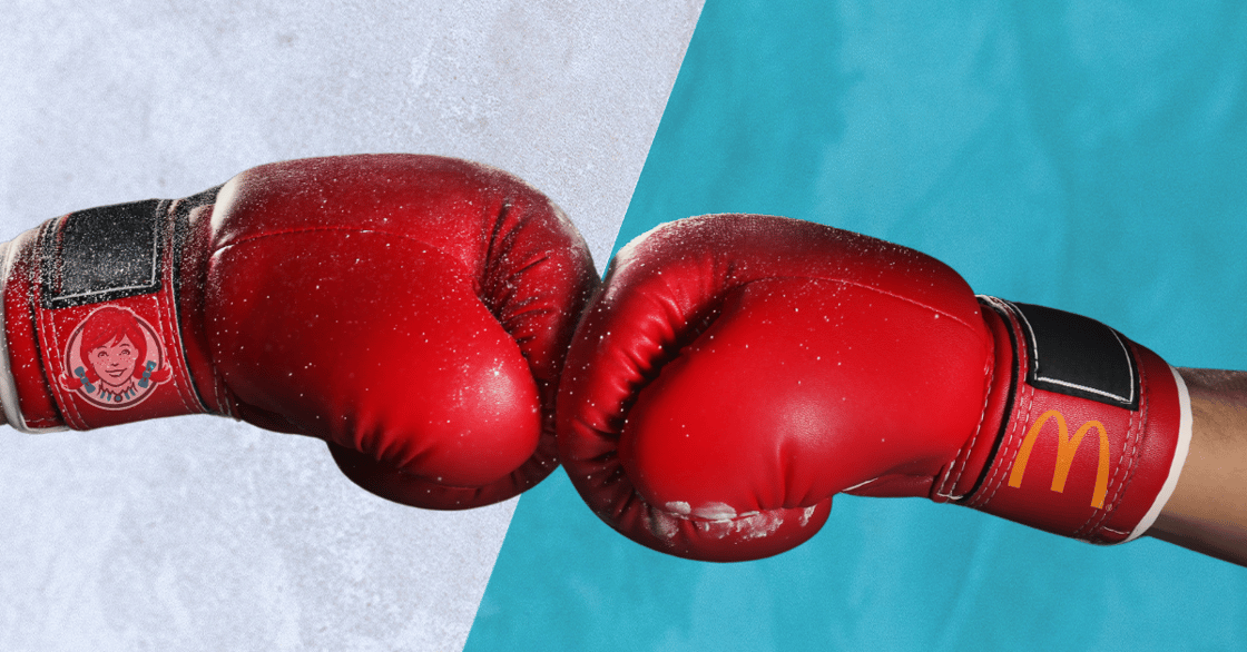 Two boxing gloves meeting from opposite sides. One shows a Wendy’s logo and one shows a McDonald’s logo.