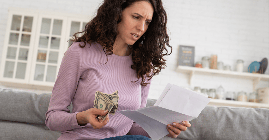 A woman appears unhappy as she holds a letter and some money.